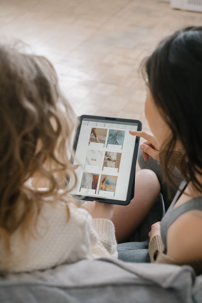about-01 Two women sitting together, shopping online using a tablet, sharing ideas and browsing products.